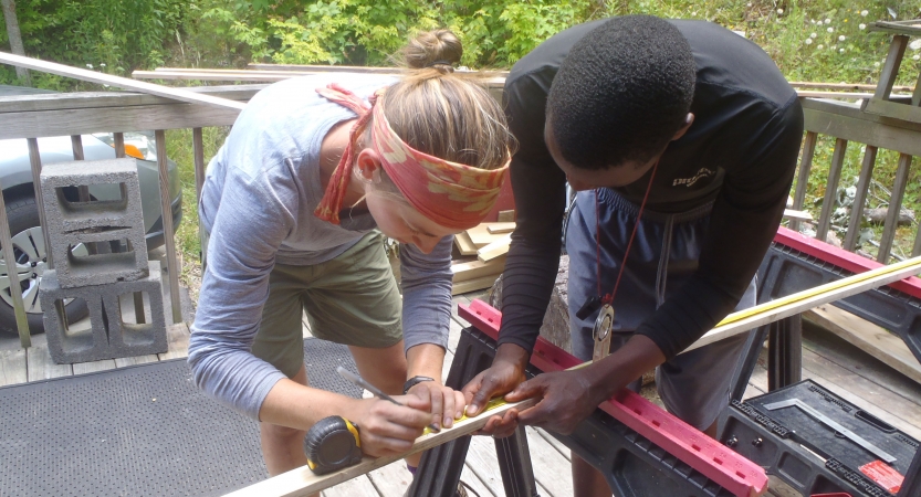Two people mark a piece of wood for cutting.